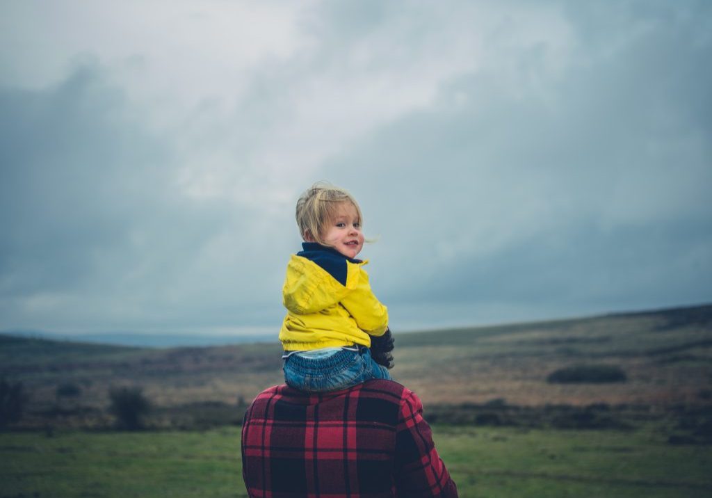 A little toddler is riding on his father's shoulders on the moor