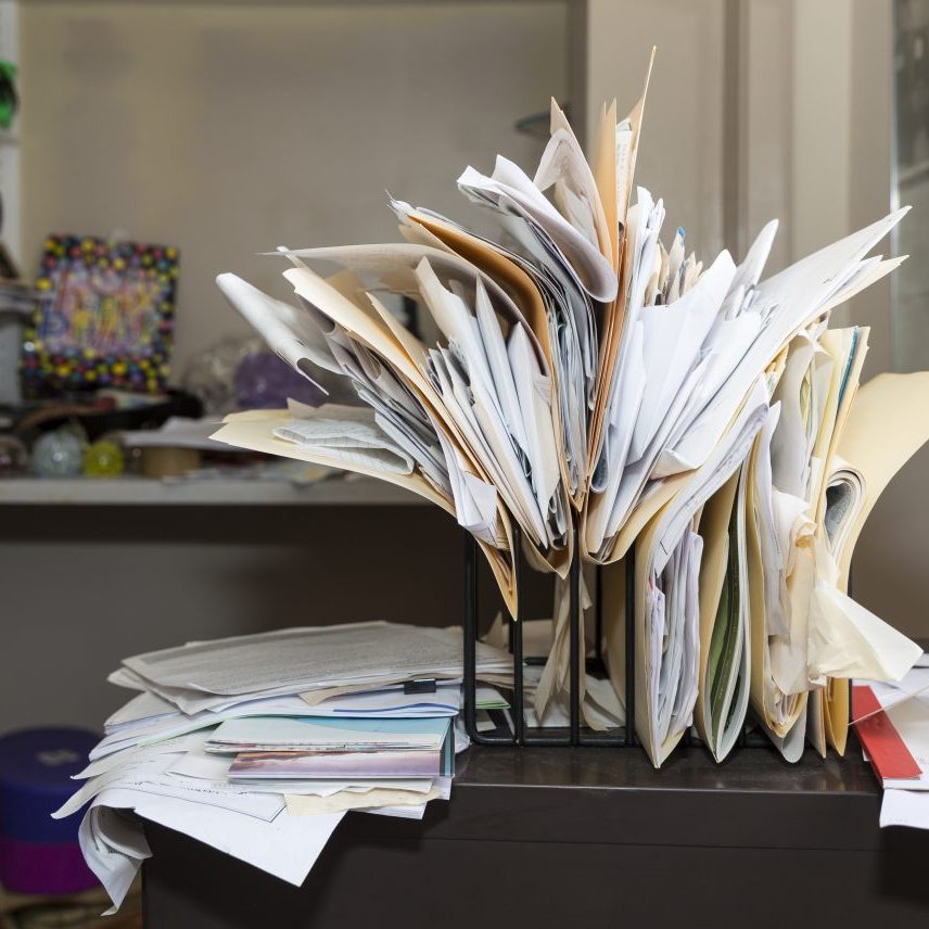 Example of desk clutter with haphazardly arranged, overstuffed file folders in a rack on a messy desk in a cluttered room. Canon EOS 5DIII, 35mm